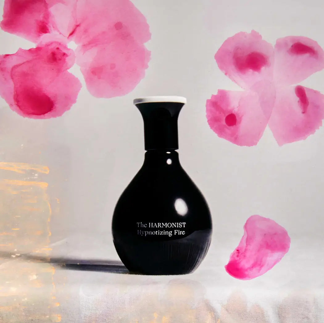 The Harmonist Hypnotizing Fire perfume bottle displayed against a soft background with watercolor-style pink flower petals.