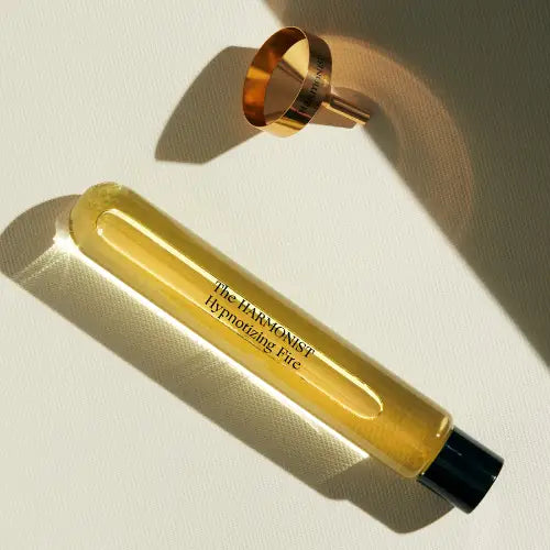 The Harmonist Hypnotizing Fire perfume refill bottle and gold ring on textured surface.
