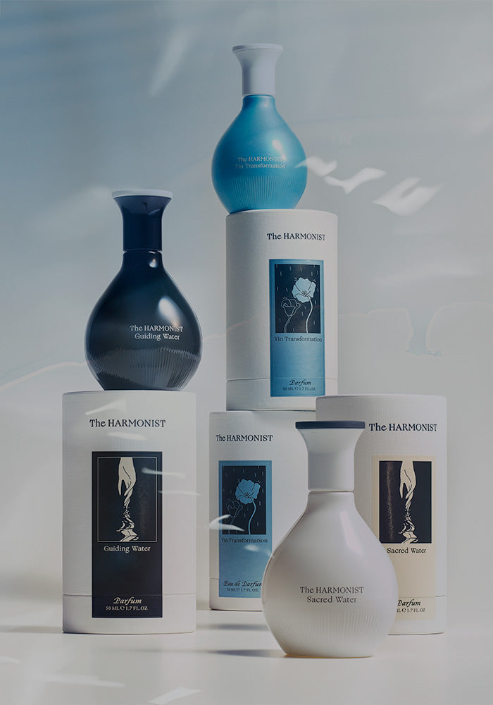 Assorted perfume bottles and packaging from The Harmonist collection, including Guiding Water, Yin Transformation, and Sacred Water, displayed on a soft, light background.