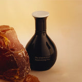 A sleek black bottle of The Harmonist's "Hypnotizing Fire" perfume, set against a warm-toned background beside a large, textured amber-hued crystal.