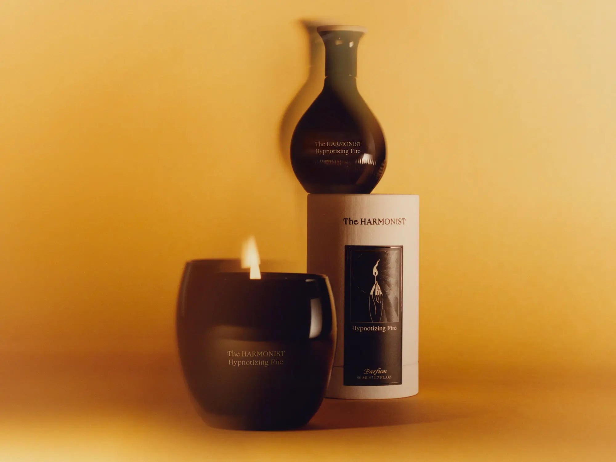Perfume bottle, candle, and packaging of "The Harmonist Hypnotizing Fire" displayed against a warm, golden background.