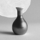 Black and white image of 'The Harmonist Moon Glory' perfume bottle with a textured moon-like background.